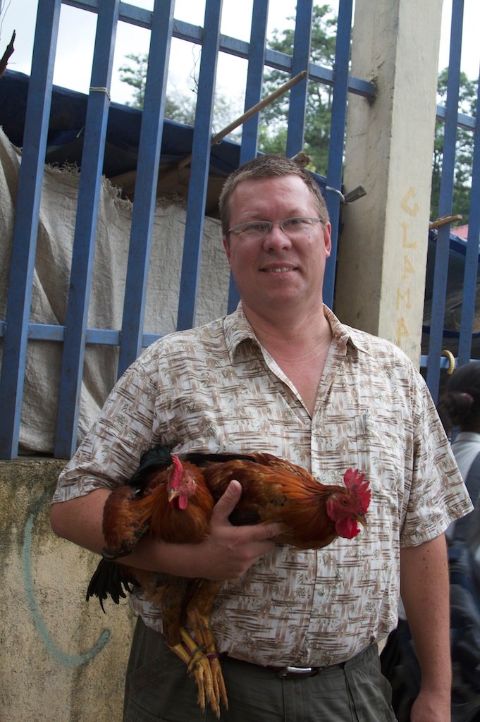 Hinrich Kaiser holding two roosters in front of a blue fence