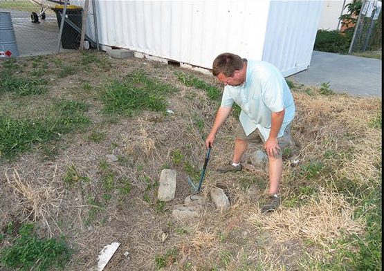 Hinrich Kaiser pointing with a snake stick at rocks beside a white airport building