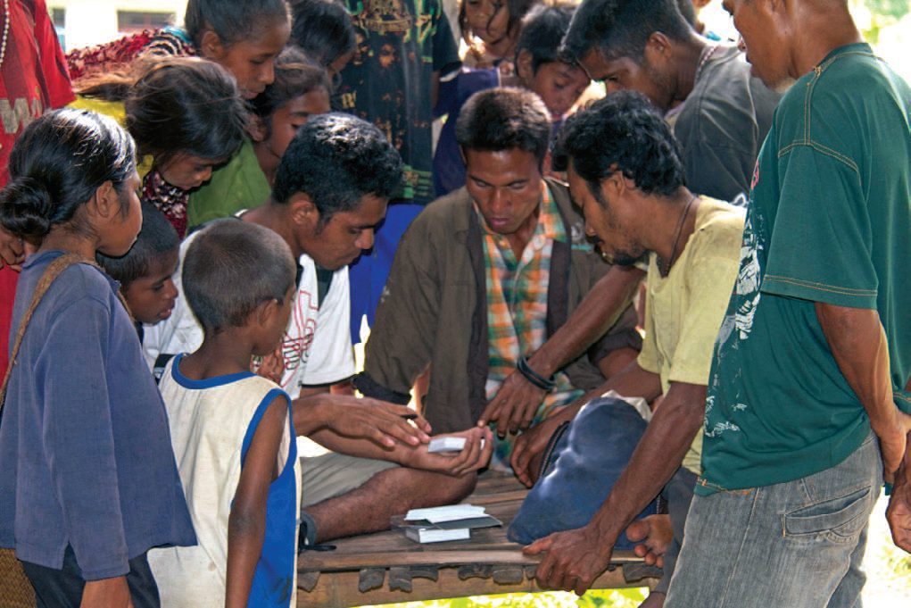 Villagers and children crowd around a table where cards are being sorted during an interview on Ataúro Island.