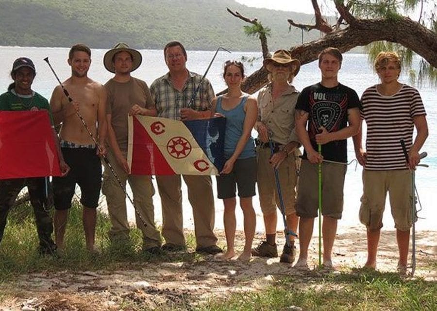 A group of field researchers on a beach holding the flag of Timor-Leste and an Explorers Club flag