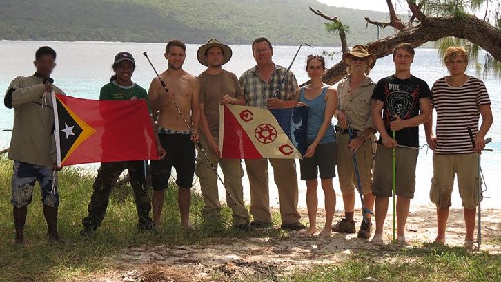 Field researchers on a beach holding the flag of Timor-Leste and an Explorers Club flag